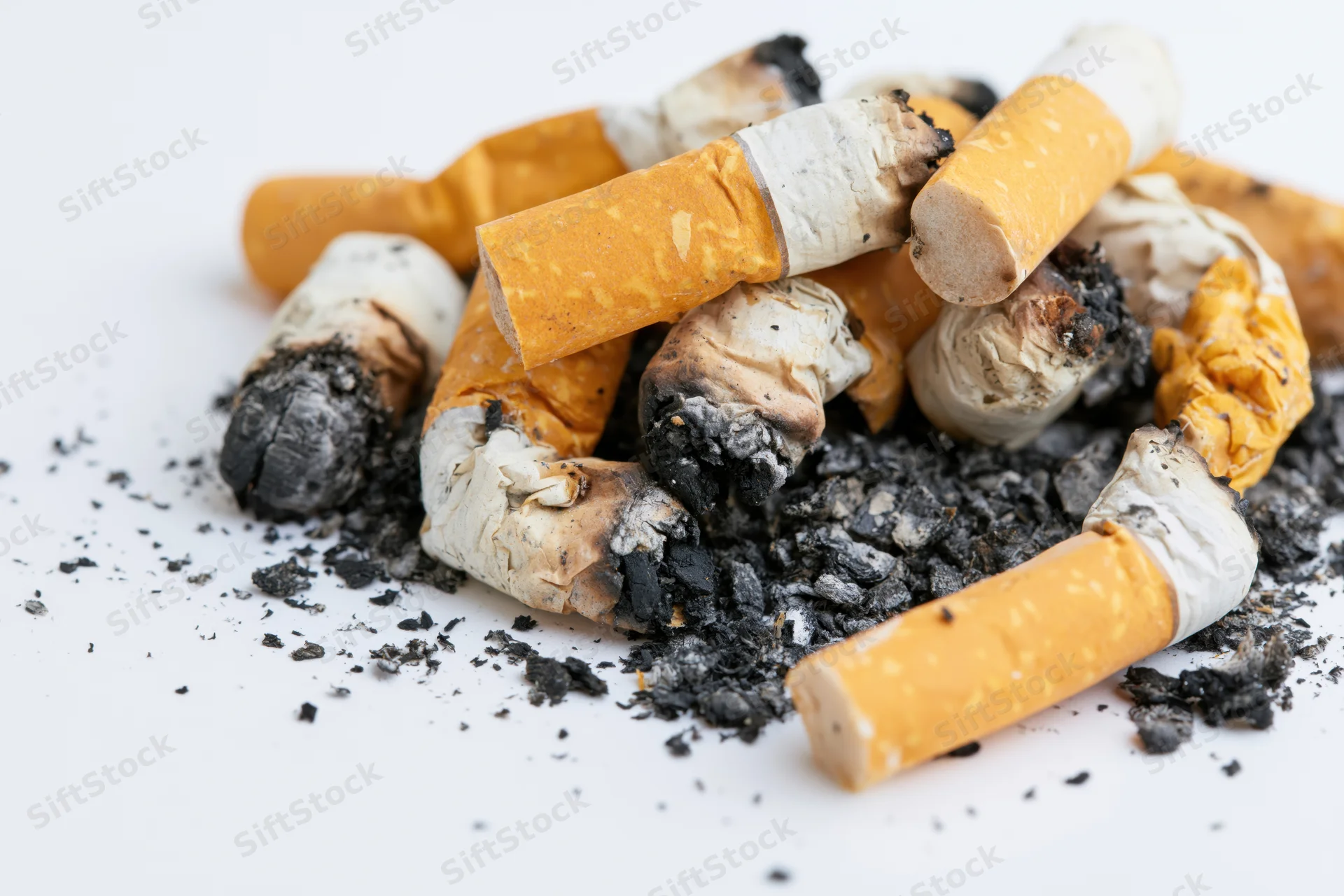 Pile of used cigarette butts with scattered ash and char on white background