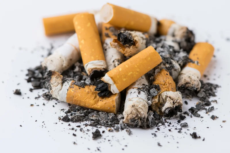 Pile of used cigarette butts with ash and char on white background