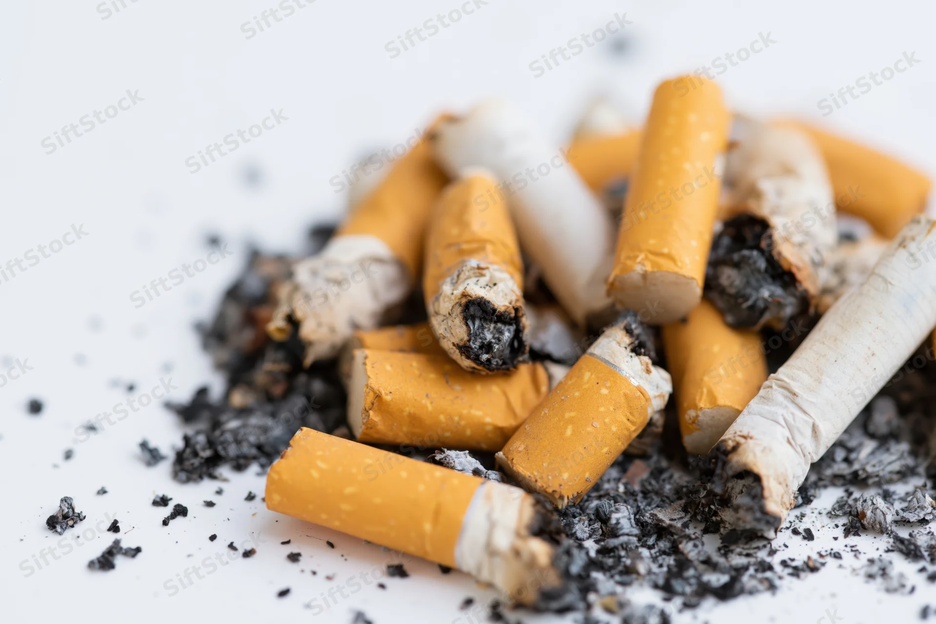 Pile of used cigarette butts with scattered ash and char on white surface
