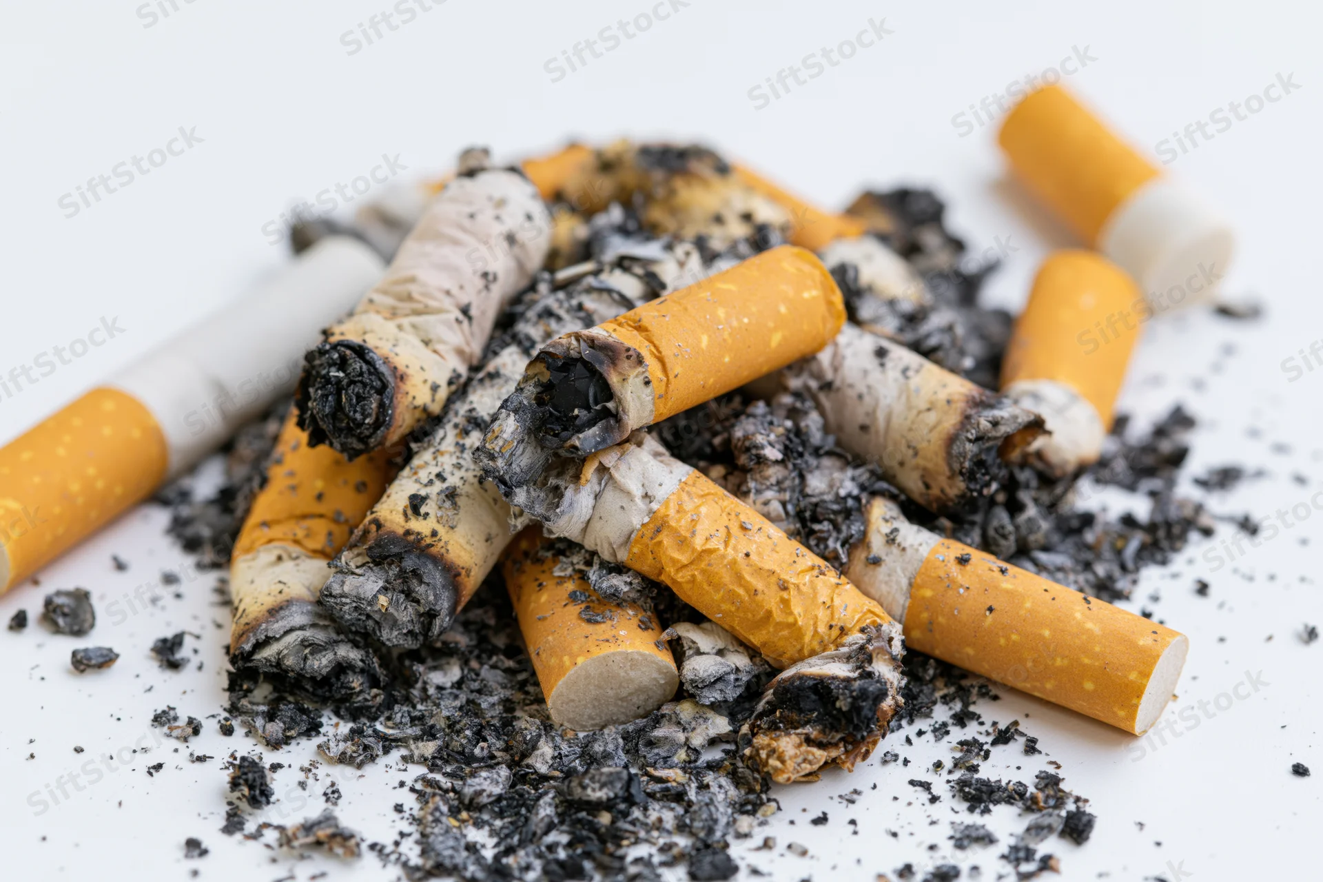 Pile of used cigarette butts with ash and char on white background