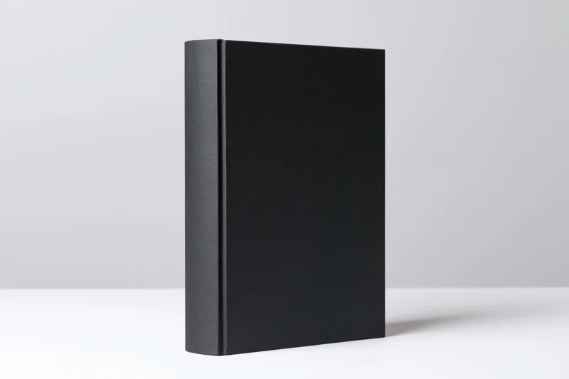 Plain black hardcover book standing upright on a white surface
