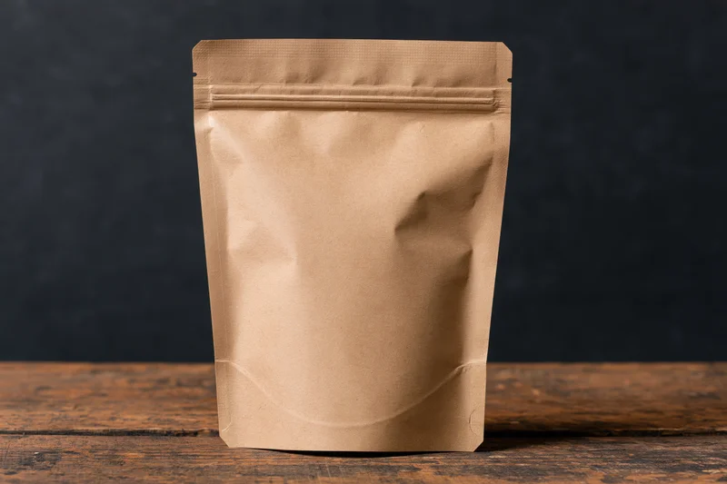 Plain kraft paper zip-lock pouch standing upright on a worn wooden table