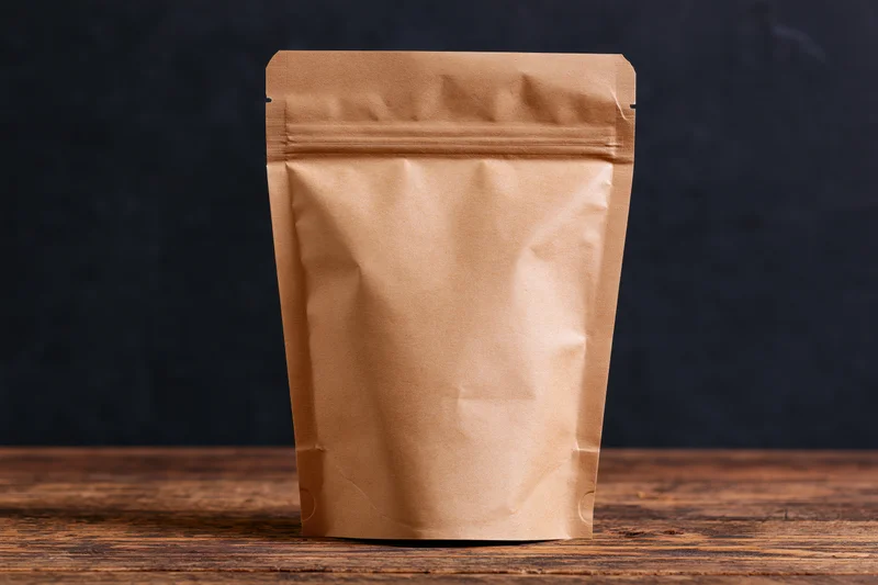 Plain kraft paper zip-lock pouch standing upright on a worn wooden table against a dark background