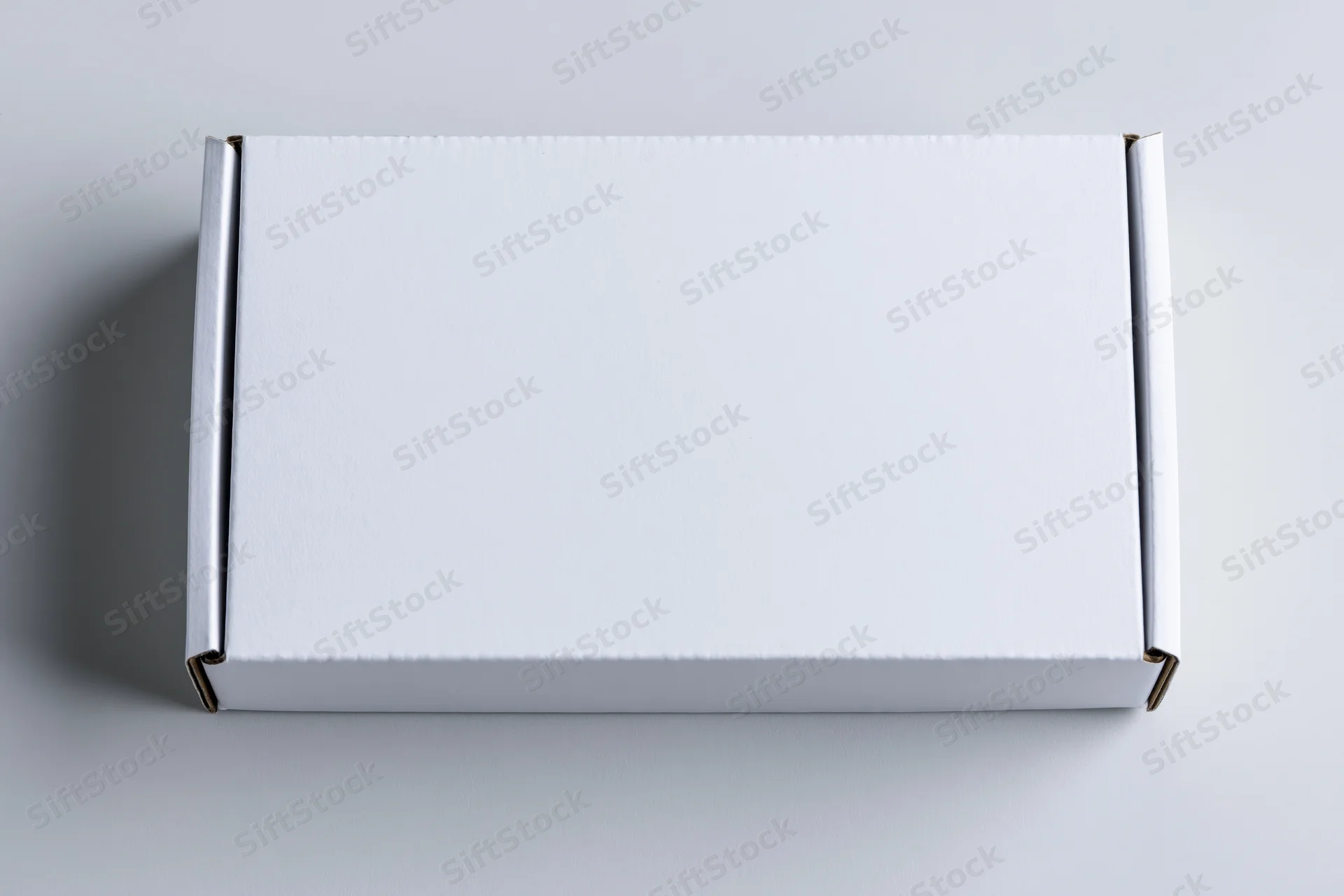 Plain white rectangular cardboard mailer box viewed from above on a neutral gray surface
