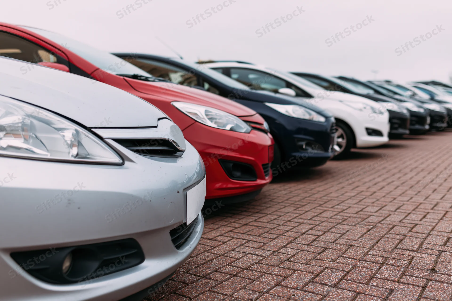 Row of compact cars parked diagonally on brick pavement