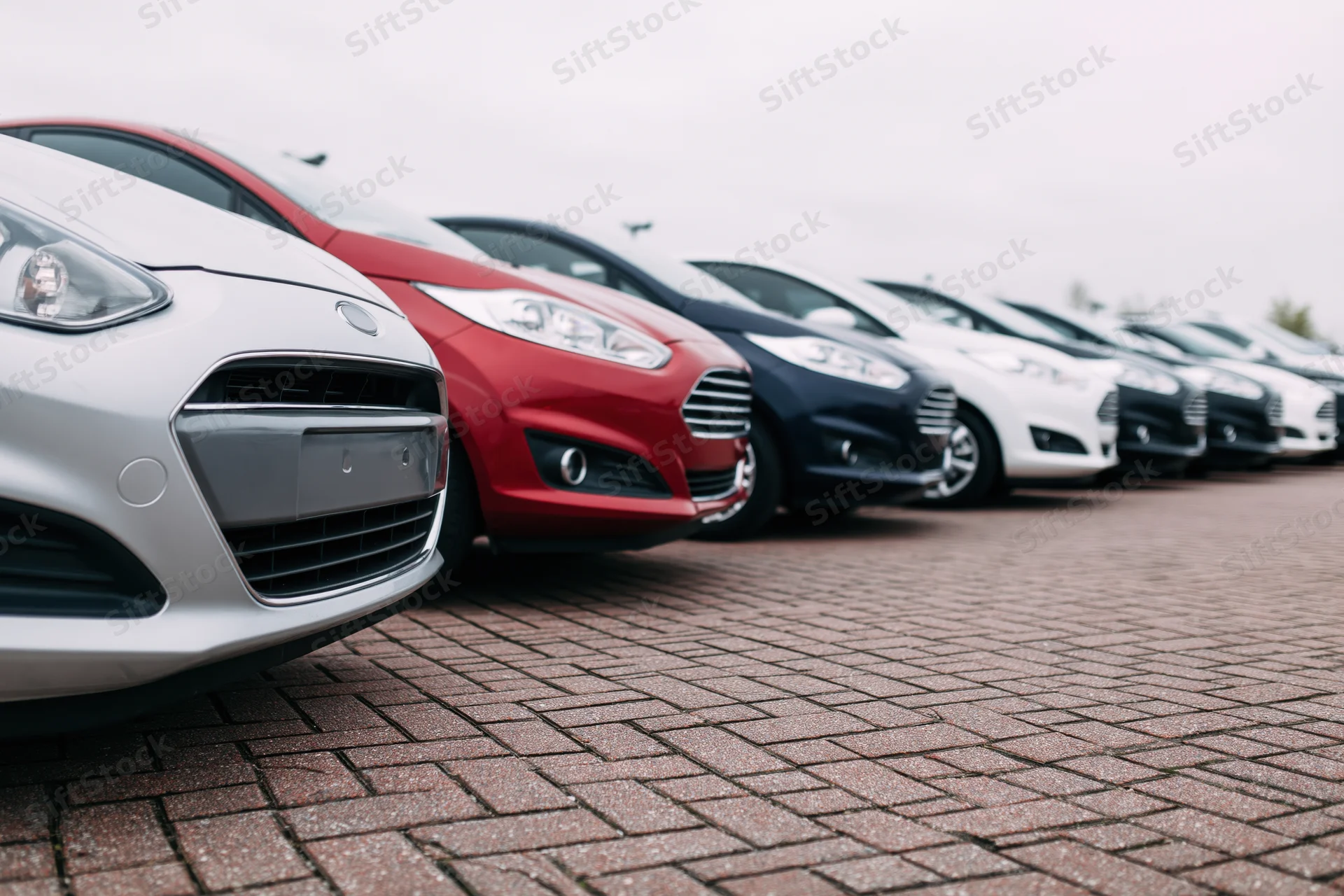 Row of compact cars parked diagonally on brick pavement