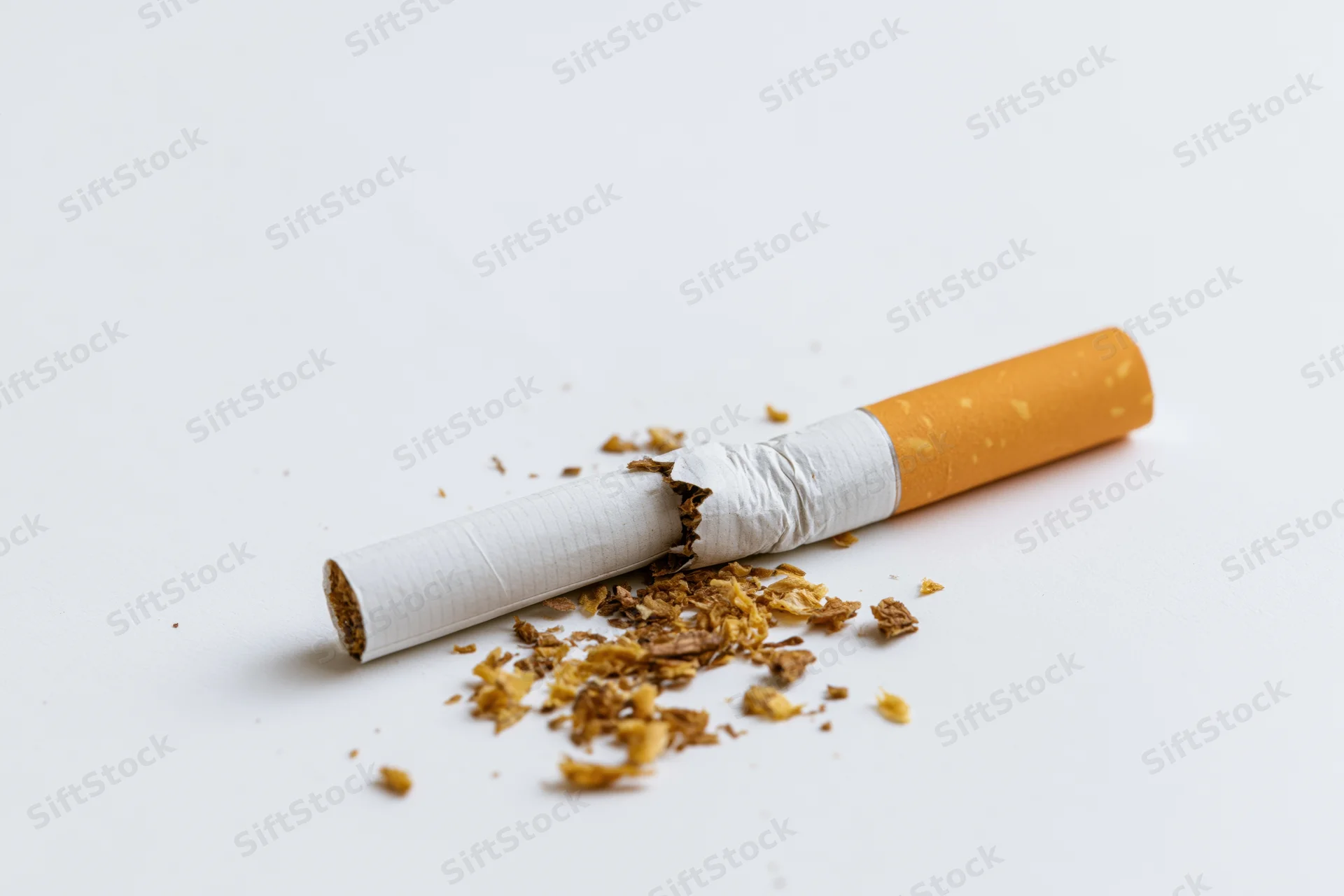 Broken cigarette lying on white surface with tobacco debris scattered around