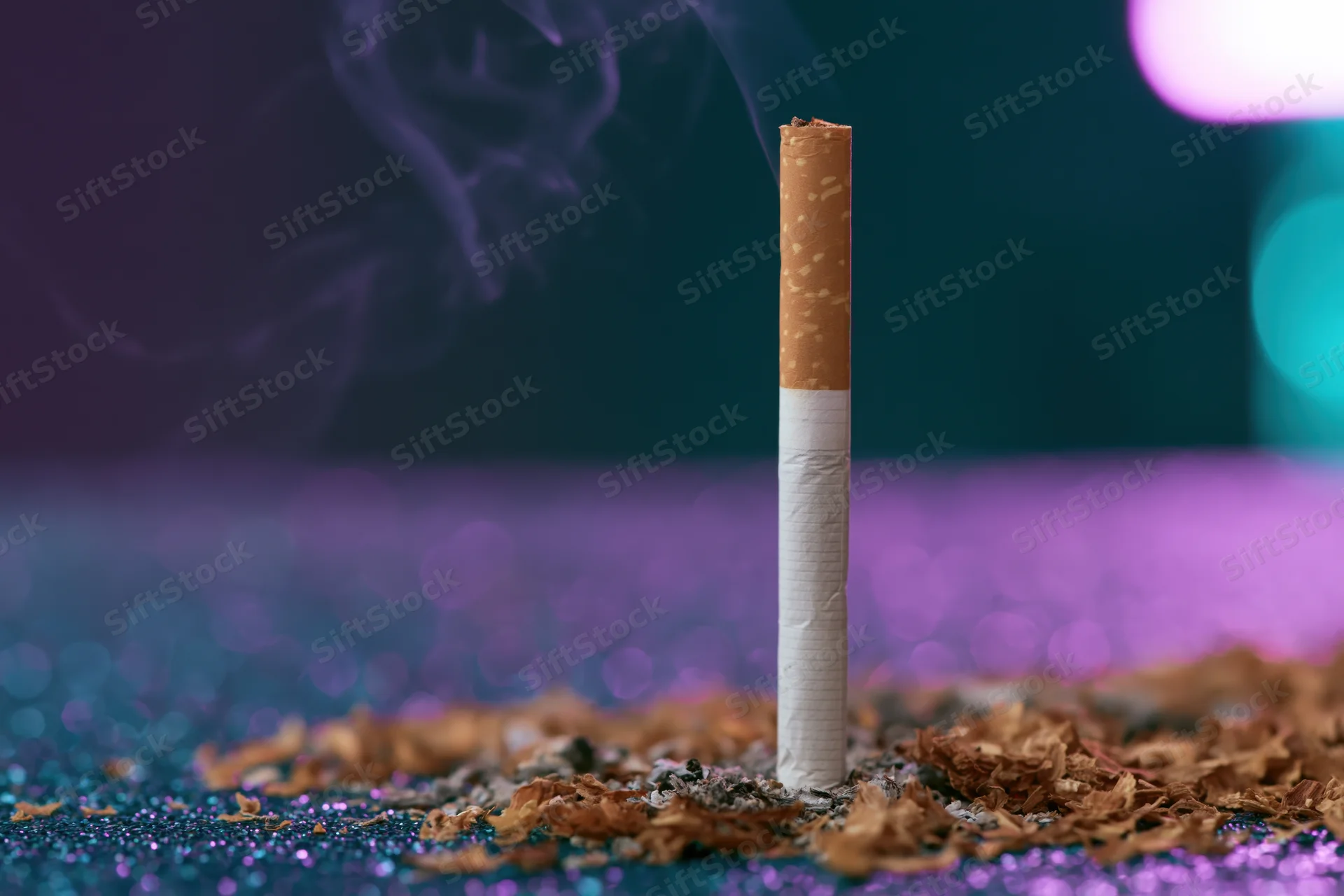 Single cigarette burning upright on glittery surface with smoke rising and colorful bokeh background