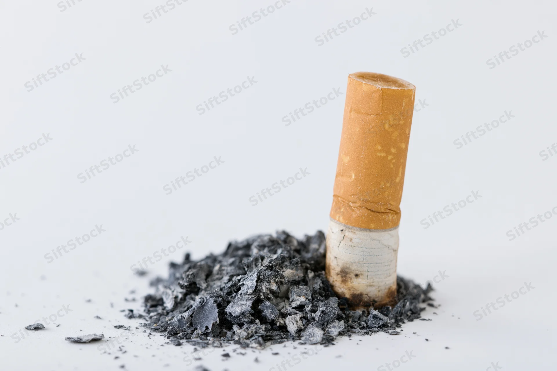 Extinguished cigarette butt standing upright in a pile of ash on a white surface