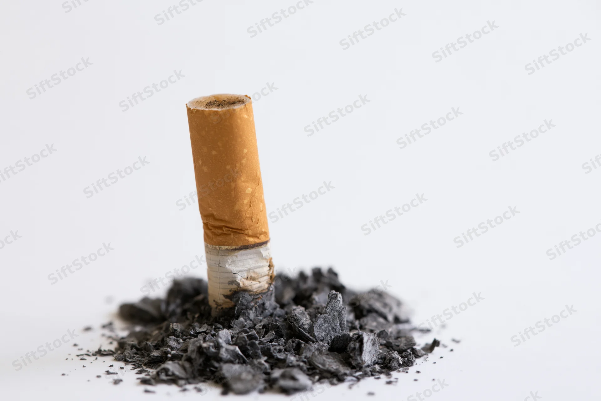 Extinguished cigarette butt standing upright on a pile of ash against a white background