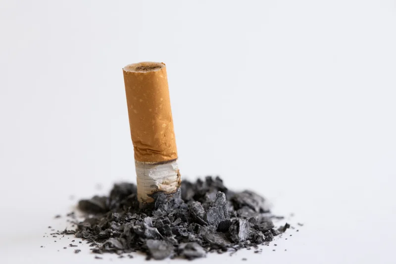 Extinguished cigarette butt standing upright on a pile of ash against a white background