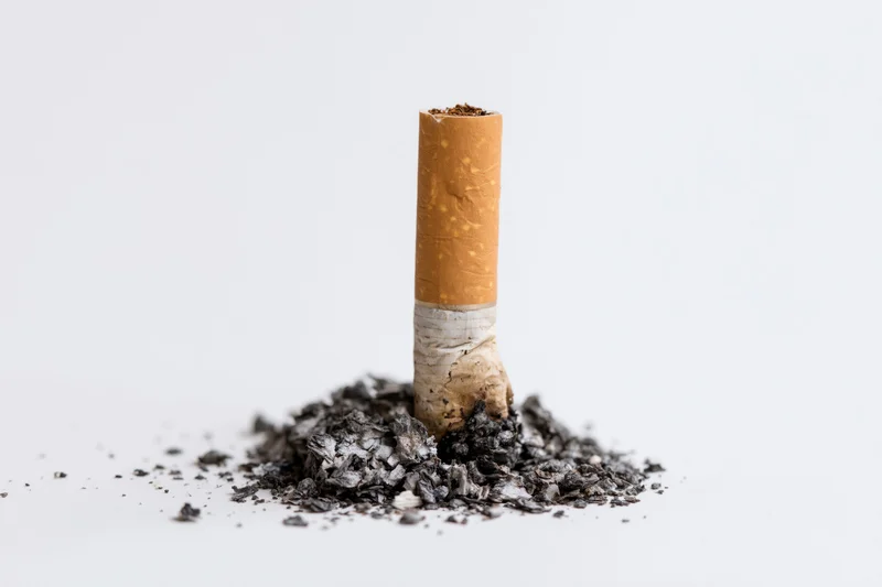 Extinguished cigarette butt standing upright in ash on white background