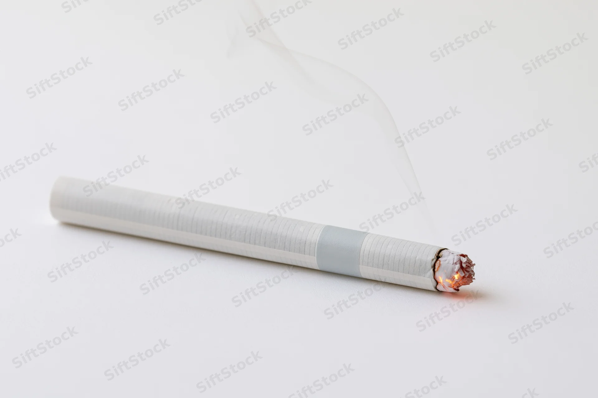 Lit cigarette lying horizontally with glowing ember and smoke on white surface