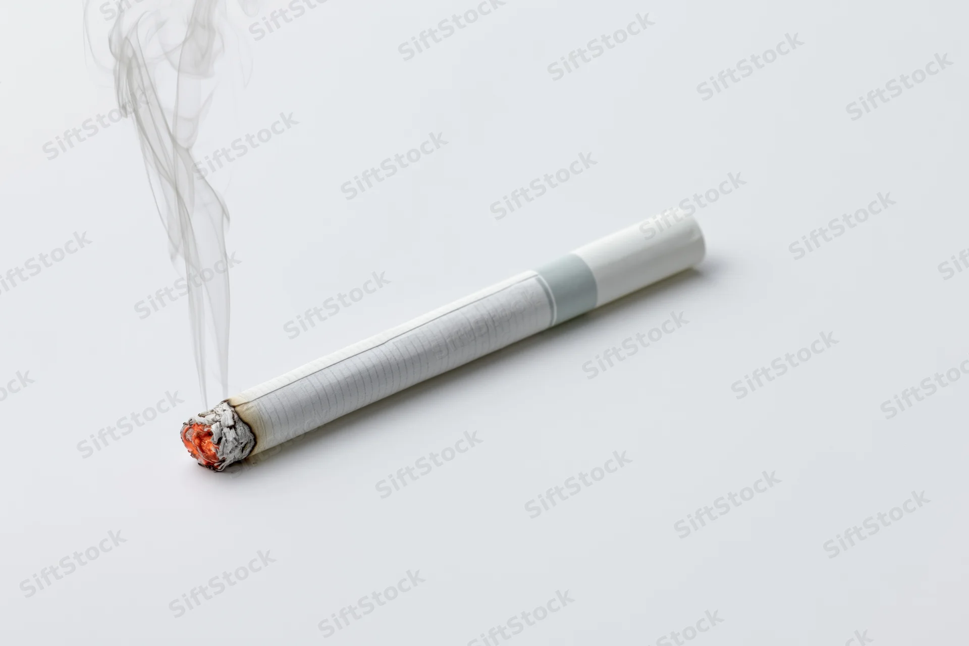 Lit cigarette burning horizontally with glowing ember and rising smoke on white surface