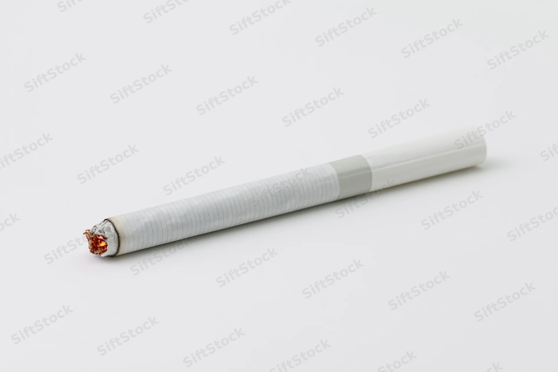 Lit cigarette lying horizontally with glowing ember on white background