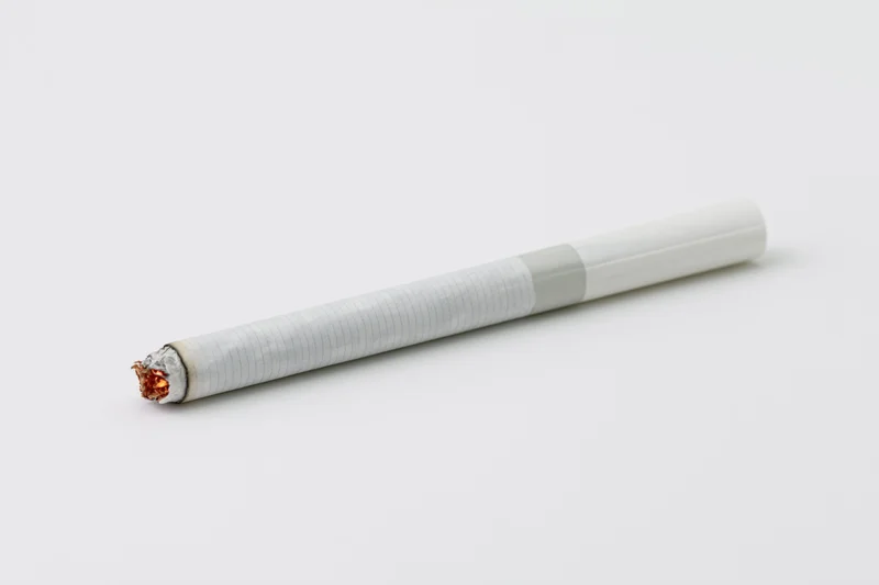 Lit cigarette lying horizontally with glowing ember on white background