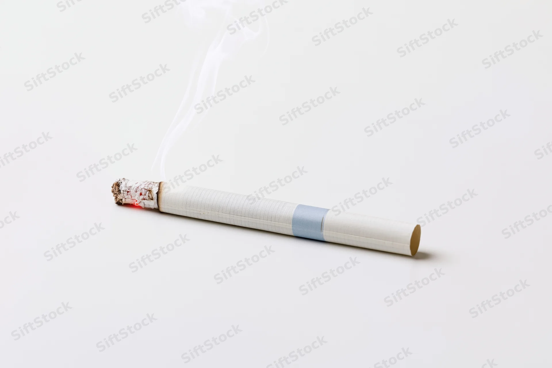Lit cigarette with smoke and ash resting horizontally on white surface
