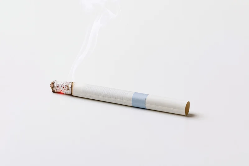 Single lit cigarette resting horizontally with white smoke
