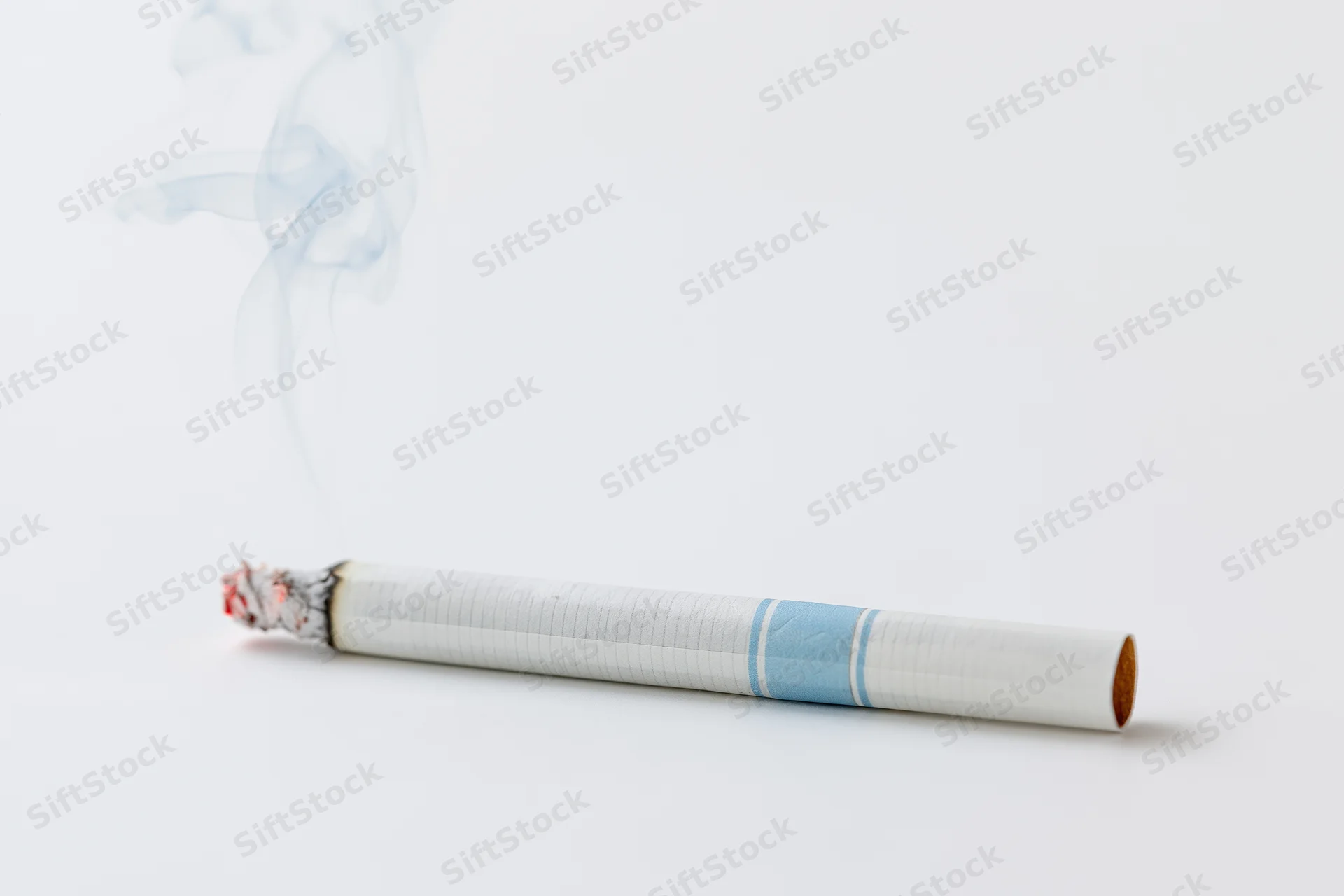Lit cigarette with smoke rising, resting horizontally on white surface