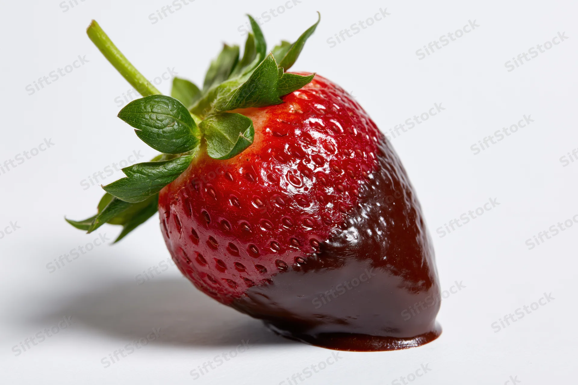 Single ripe strawberry half-dipped in dark chocolate on white surface