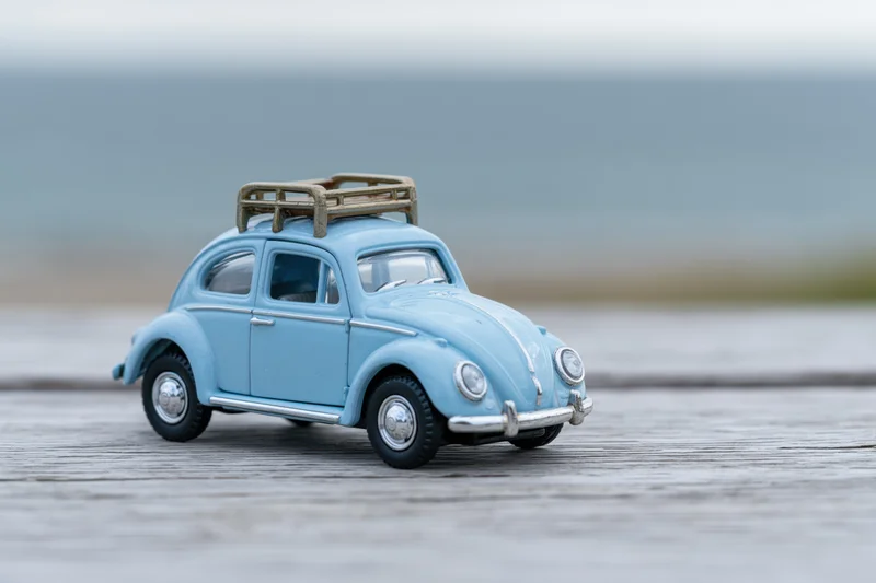 Blue vintage toy beetle with wooden roof rack on wooden deck near ocean