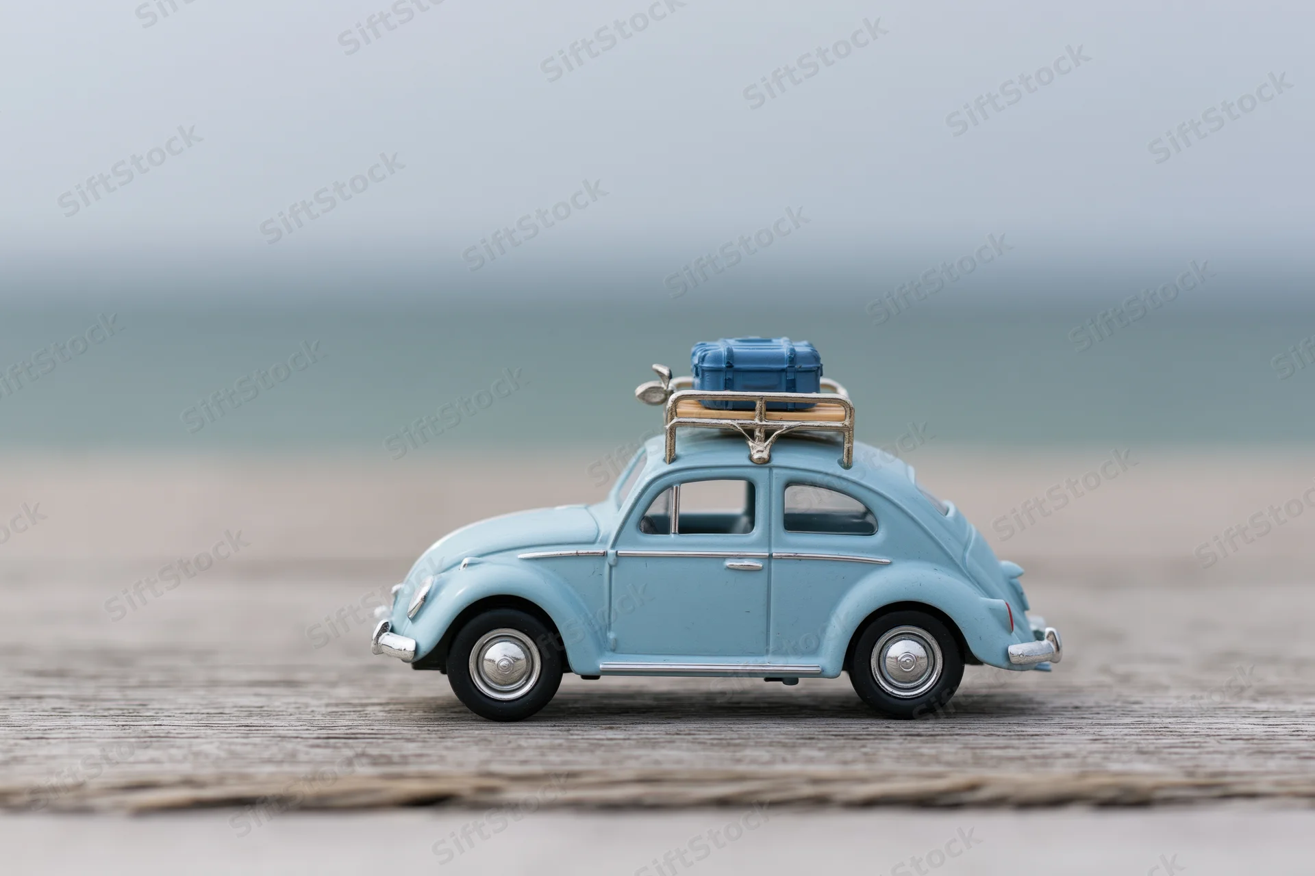 Small blue vintage toy car with luggage rack on wooden surface near beach