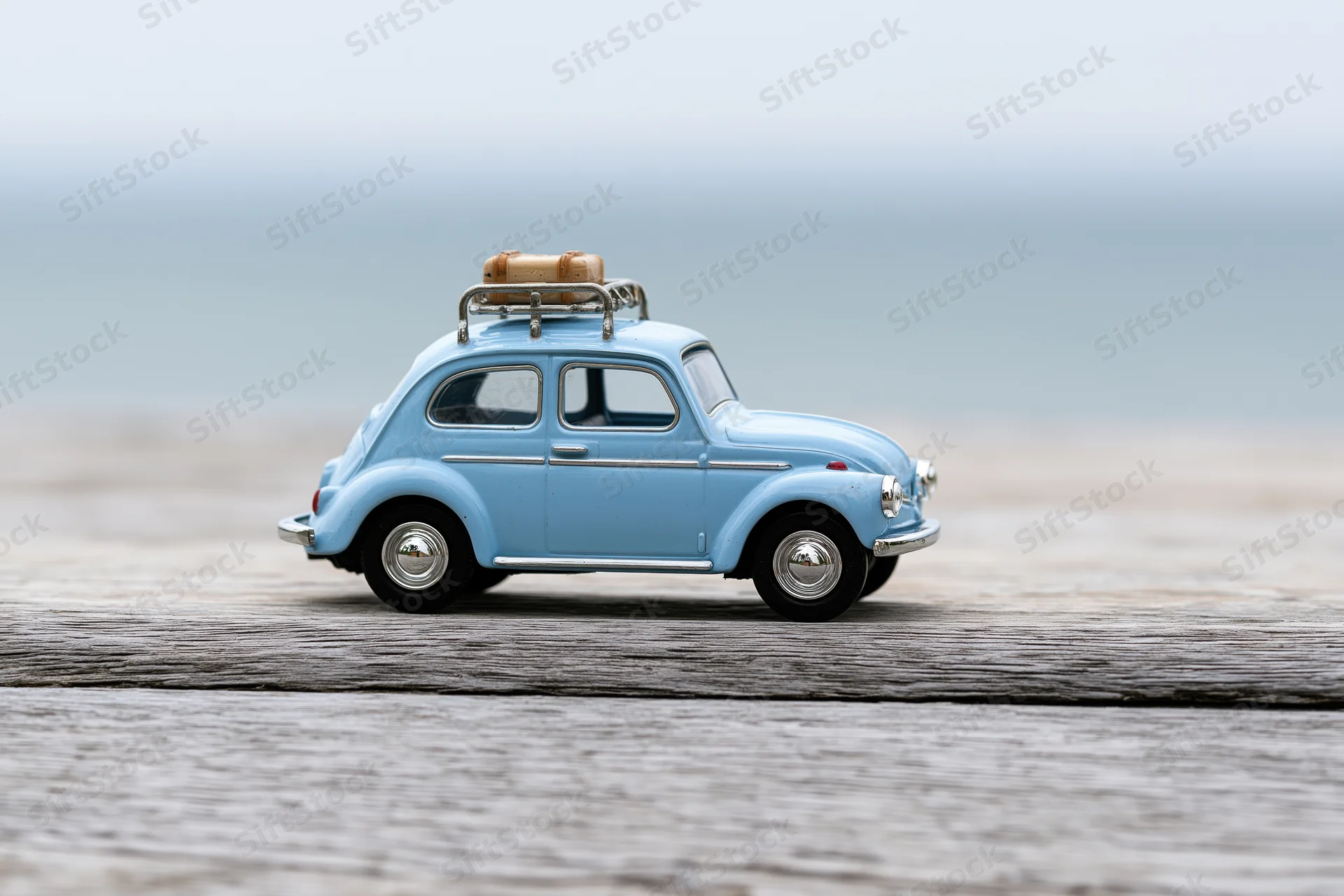 Blue vintage toy beetle with luggage rack on wooden deck near ocean