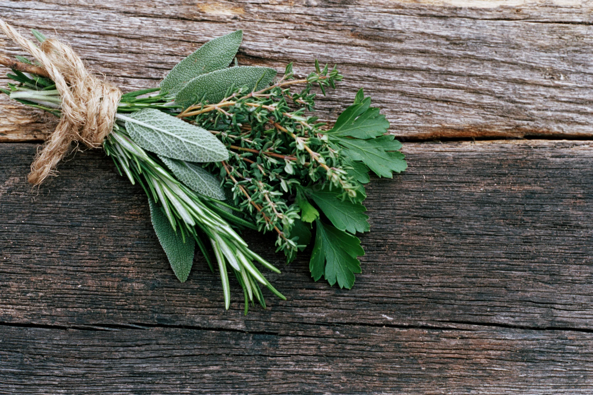 A bundle of fresh sage rosemary thyme and parsley tied with twine on a rustic wooden surface