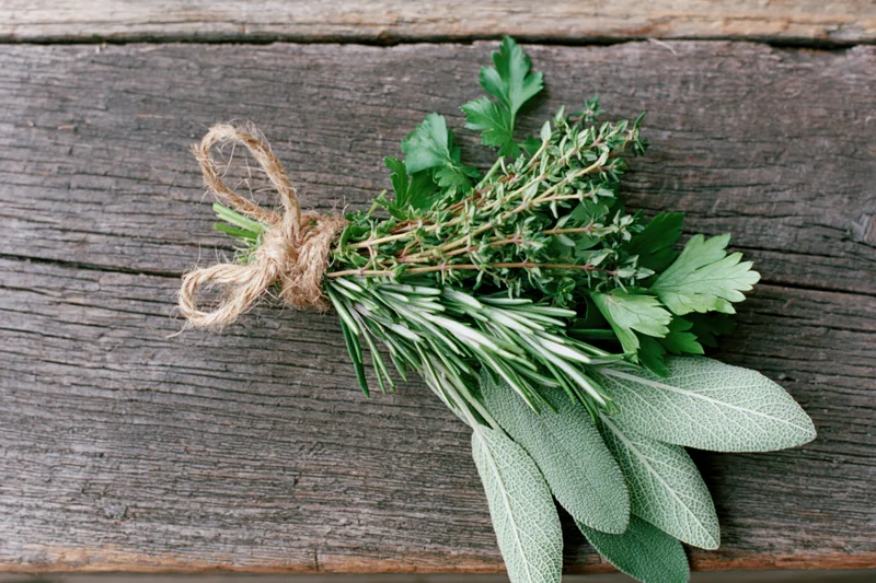 A bundle of fresh herbs including rosemary, sage, thyme, and parsley tied with twine on a weathered wooden surface