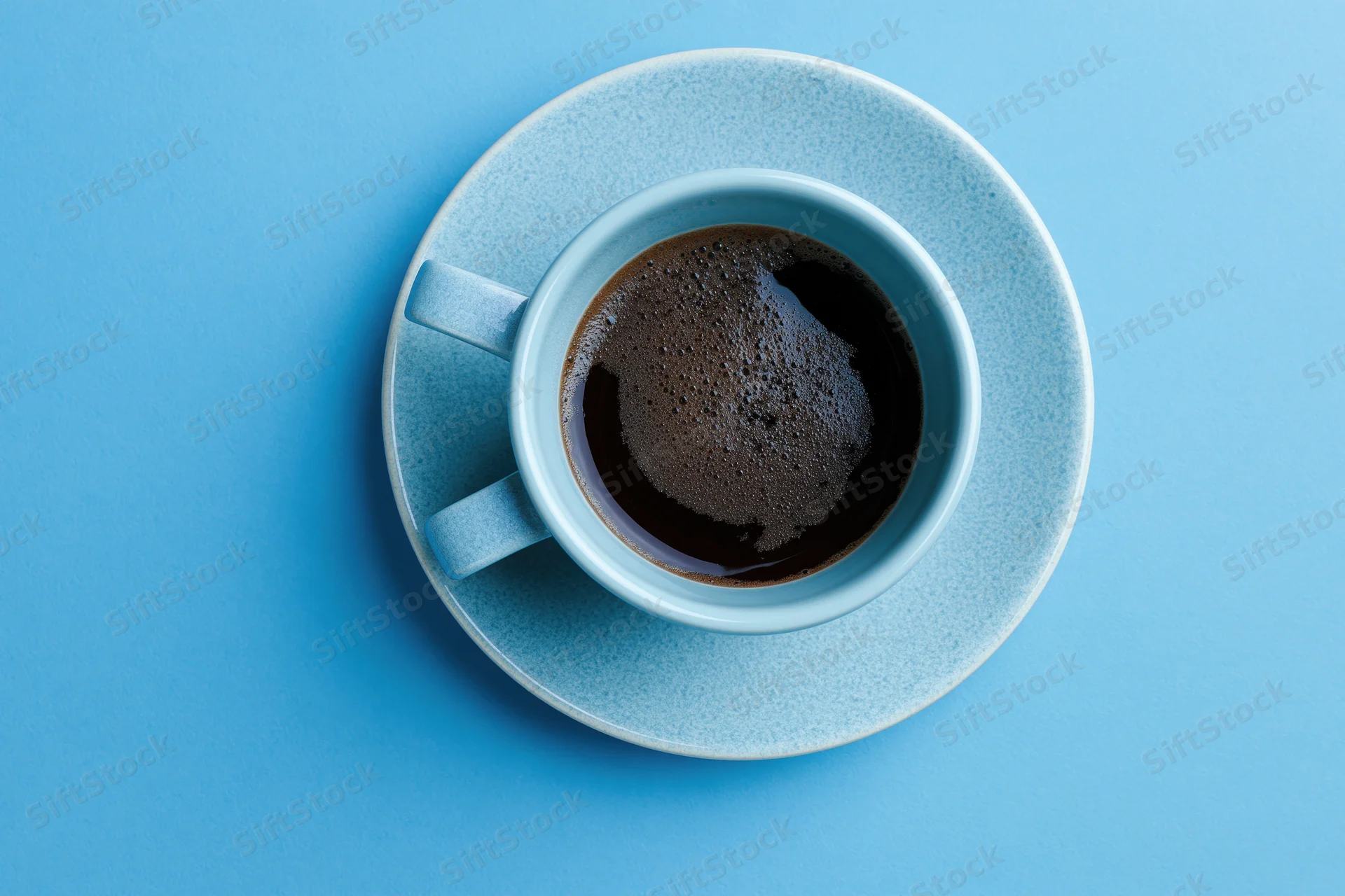 Small light-blue ceramic cup filled with black espresso on matching saucer against solid blue background, top-down view