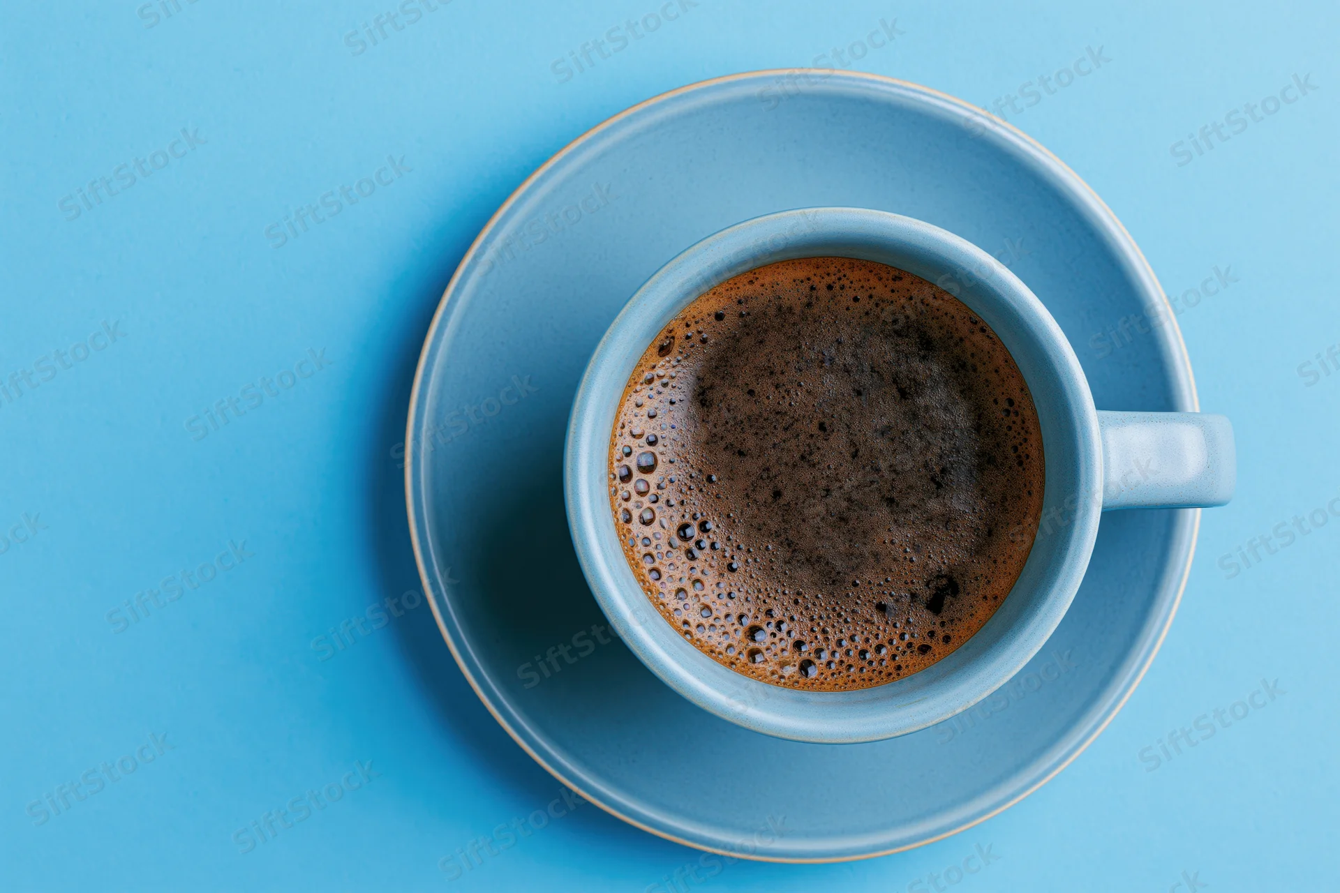 Black espresso in a light-blue ceramic cup on matching saucer, overhead view on blue surface