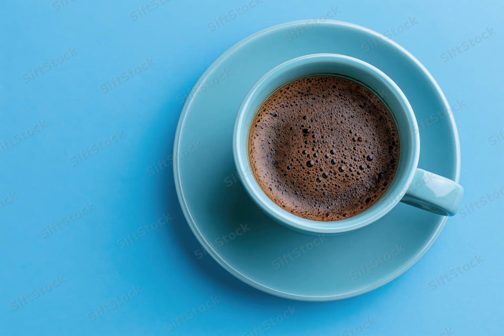 Light-blue ceramic cup filled with black espresso on matching saucer against solid blue background, viewed from above