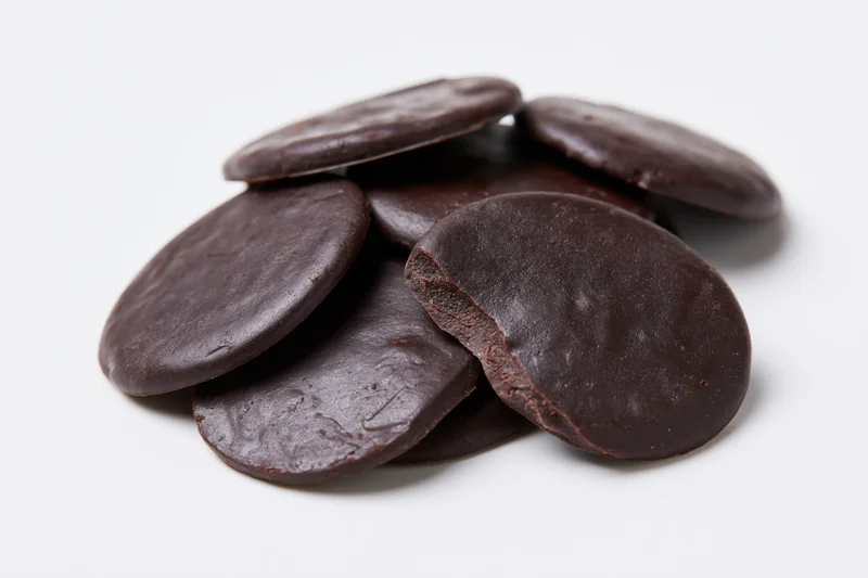 Dark chocolate discs piled on a white surface