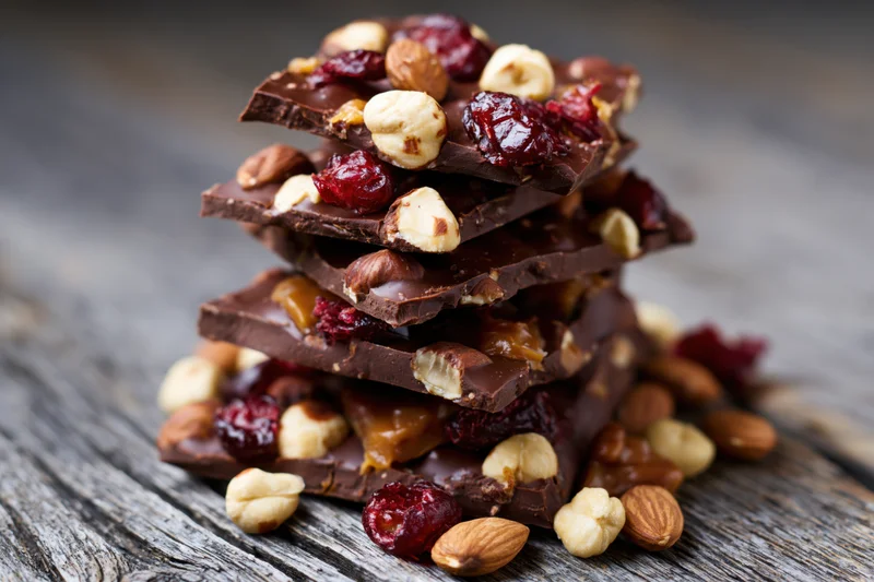 Stack of chocolate bark pieces with nuts and dried cranberries on wooden surface