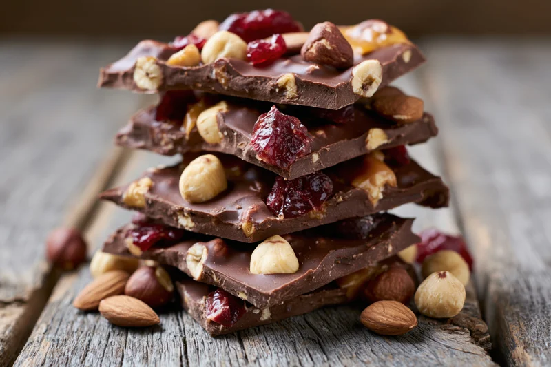 Stack of chocolate bark with hazelnuts, almonds and dried cranberries on a rustic wooden surface