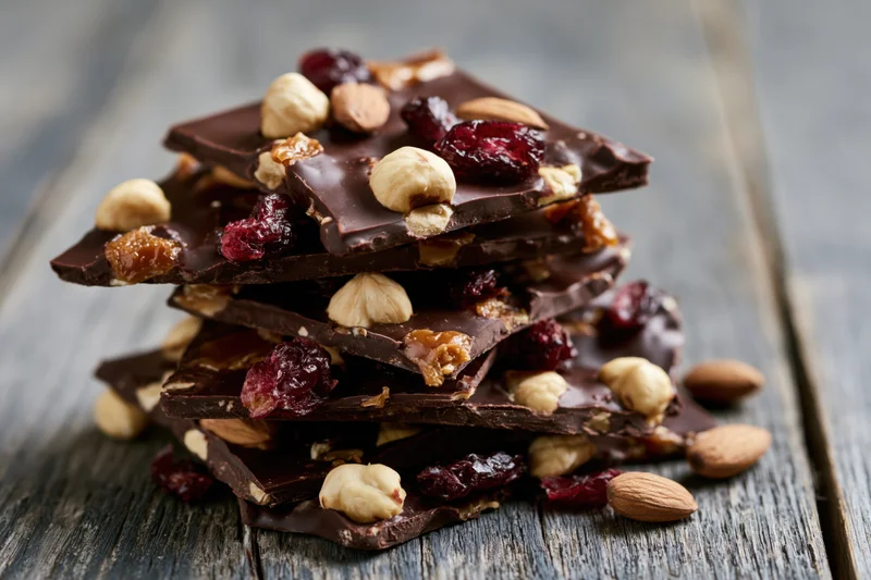 Stack of chocolate bark with nuts and dried cranberries on wooden surface