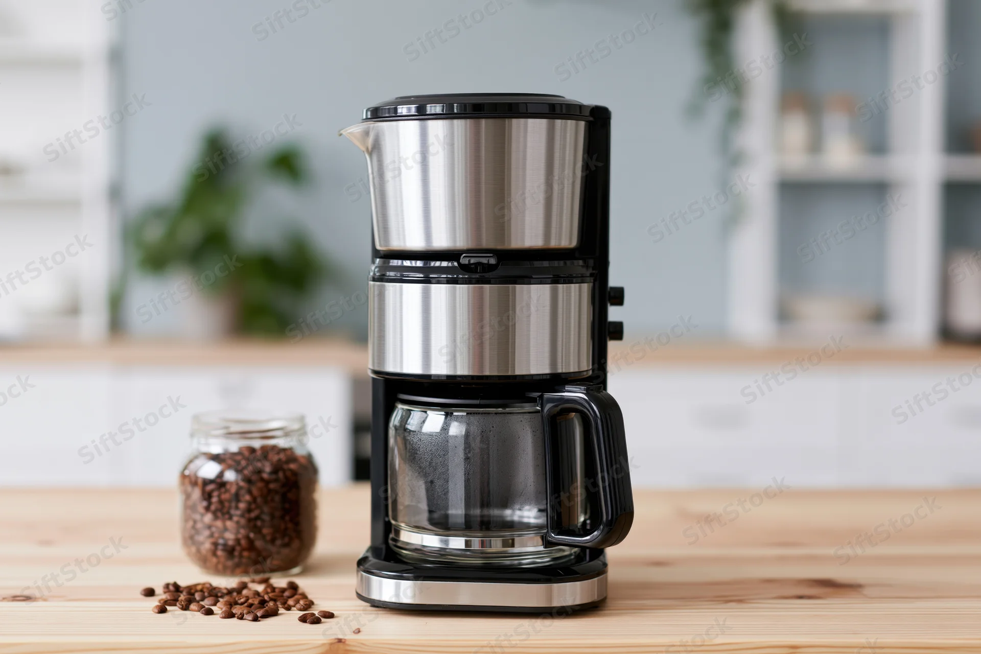 Stainless steel and black drip coffee maker on wooden kitchen countertop with coffee beans in glass jar nearby