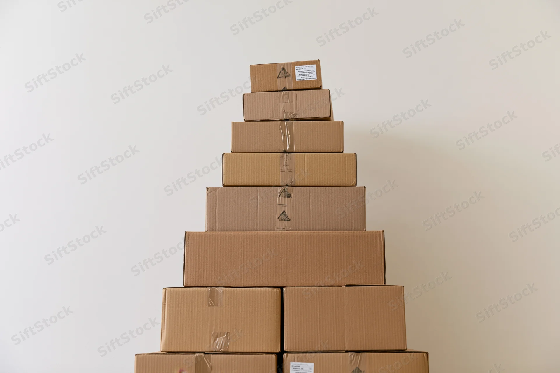 Pyramid-shaped stack of cardboard shipping boxes against a plain wall