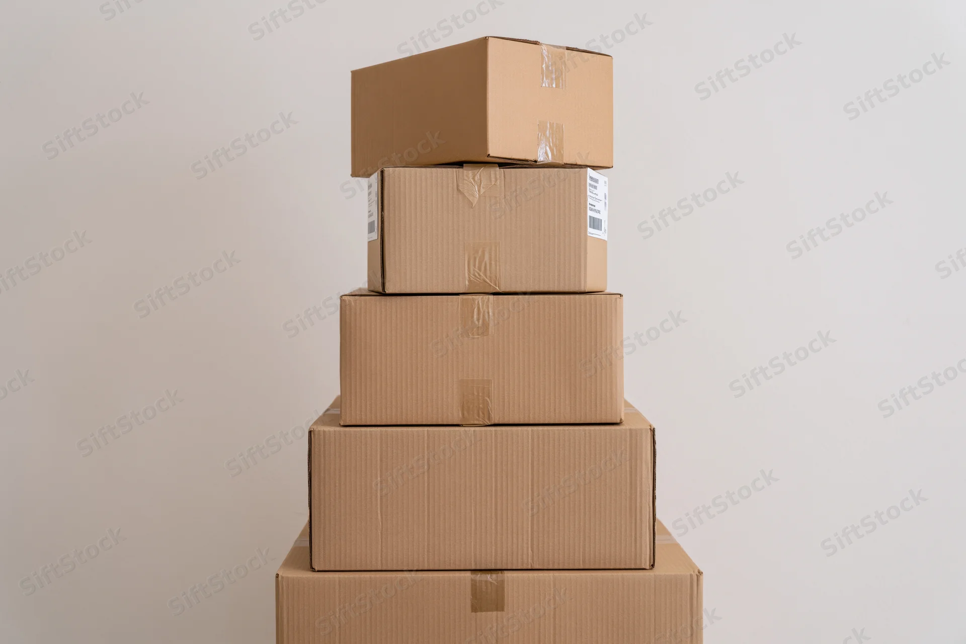 Pyramid stack of cardboard shipping boxes arranged vertically against a plain wall