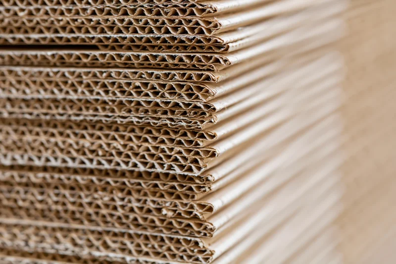 Tall stack of corrugated cardboard sheets arranged vertically in a warehouse setting