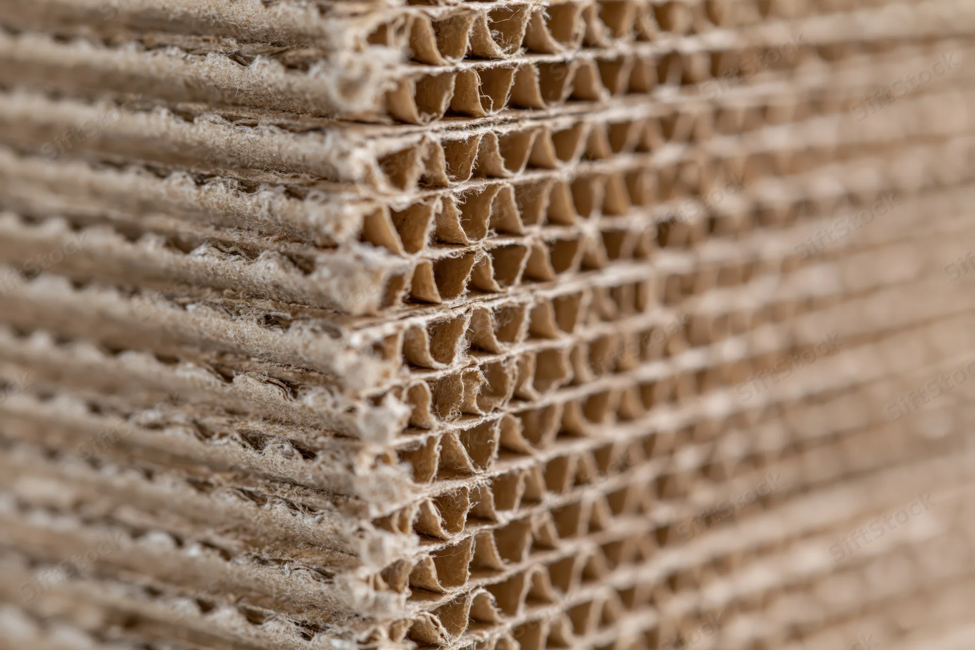 Tall stack of corrugated cardboard sheets arranged vertically with visible fluting and rough edges