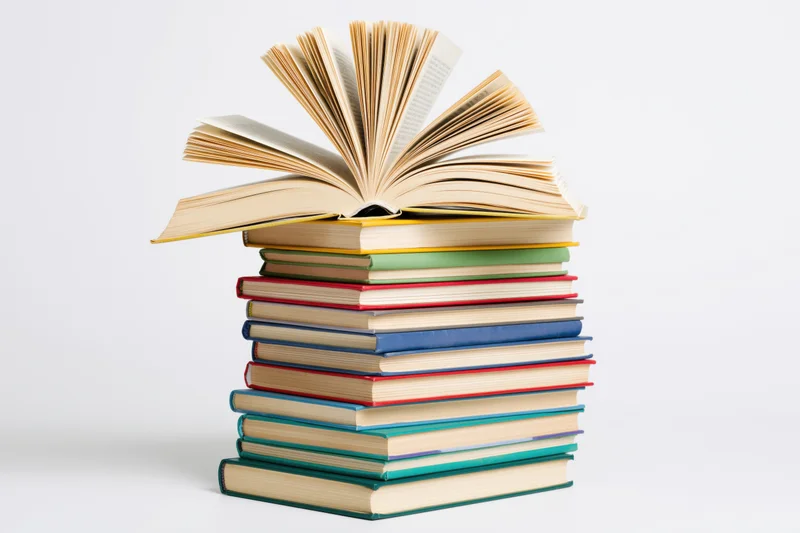 Tall stack of colorful hardcover books with one open on top against white background