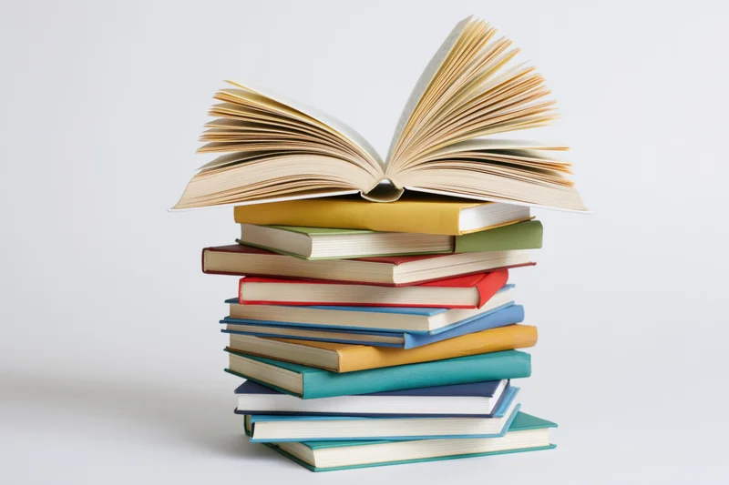Tall stack of colorful hardcover books with one open on top, isolated on white background