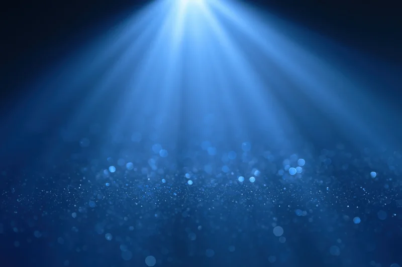 Blue light burst radiating upward from center with sparkling particles and bokeh effect in dark background