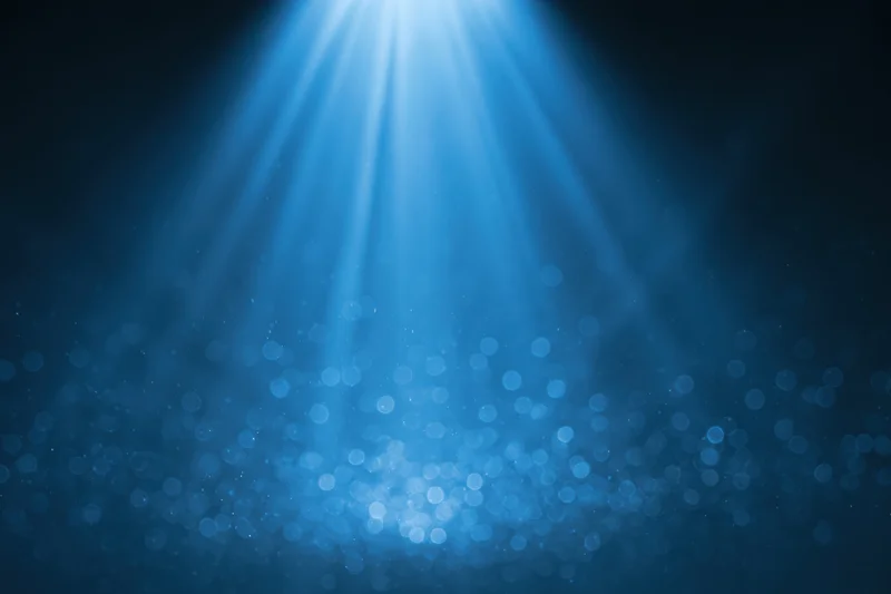 Blue light burst radiating upward from a central point in a dark space with bokeh particles
