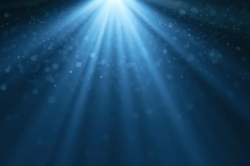 Blue light burst radiating upward from a central point in a dark abstract background with bokeh particles
