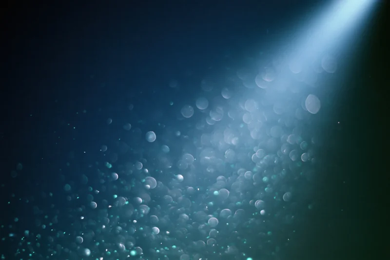 Floating out-of-focus light particles in dark blue abstract background with soft glow and bokeh effect