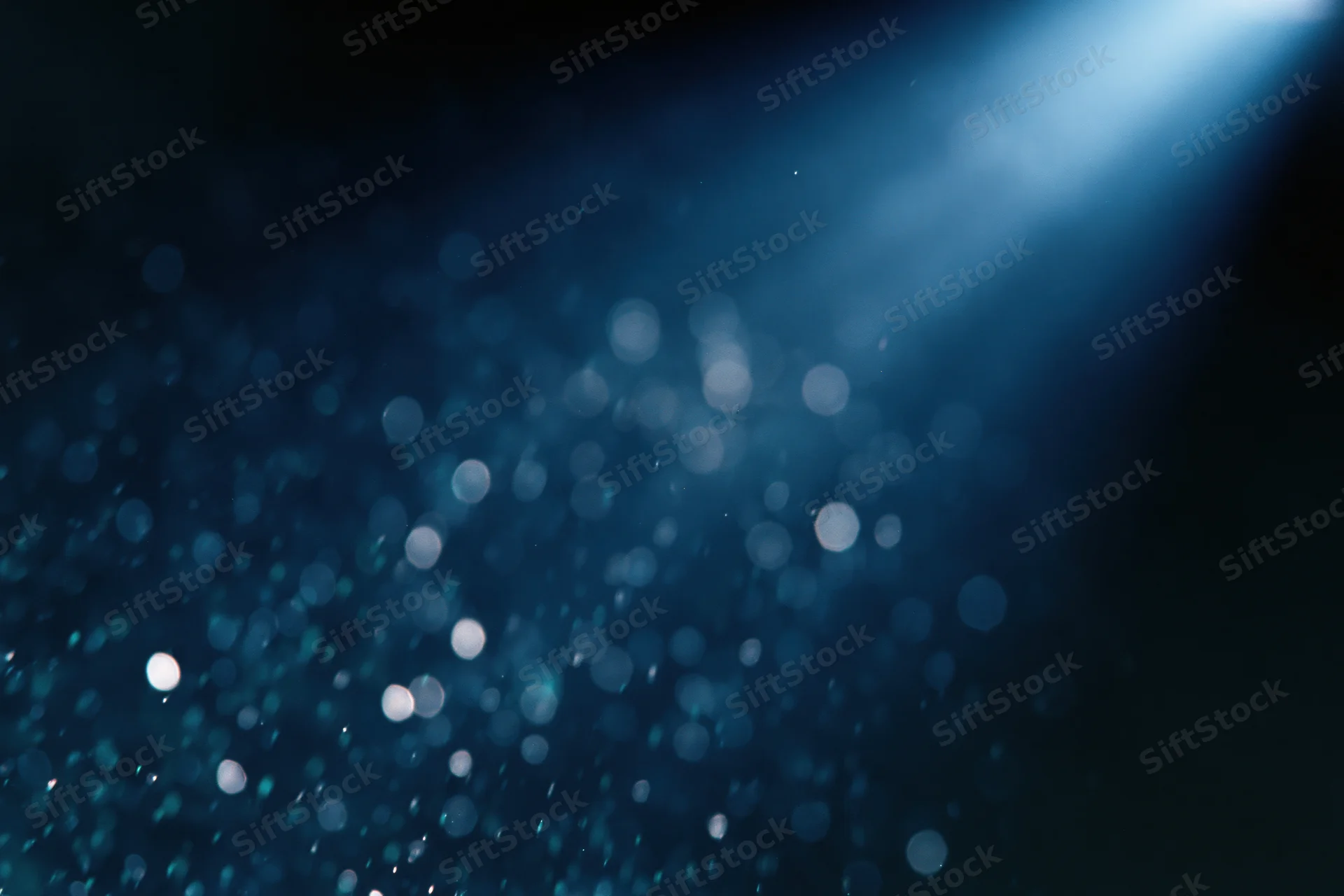 Floating out-of-focus light particles in dark blue abstract background with soft glow and bokeh effect