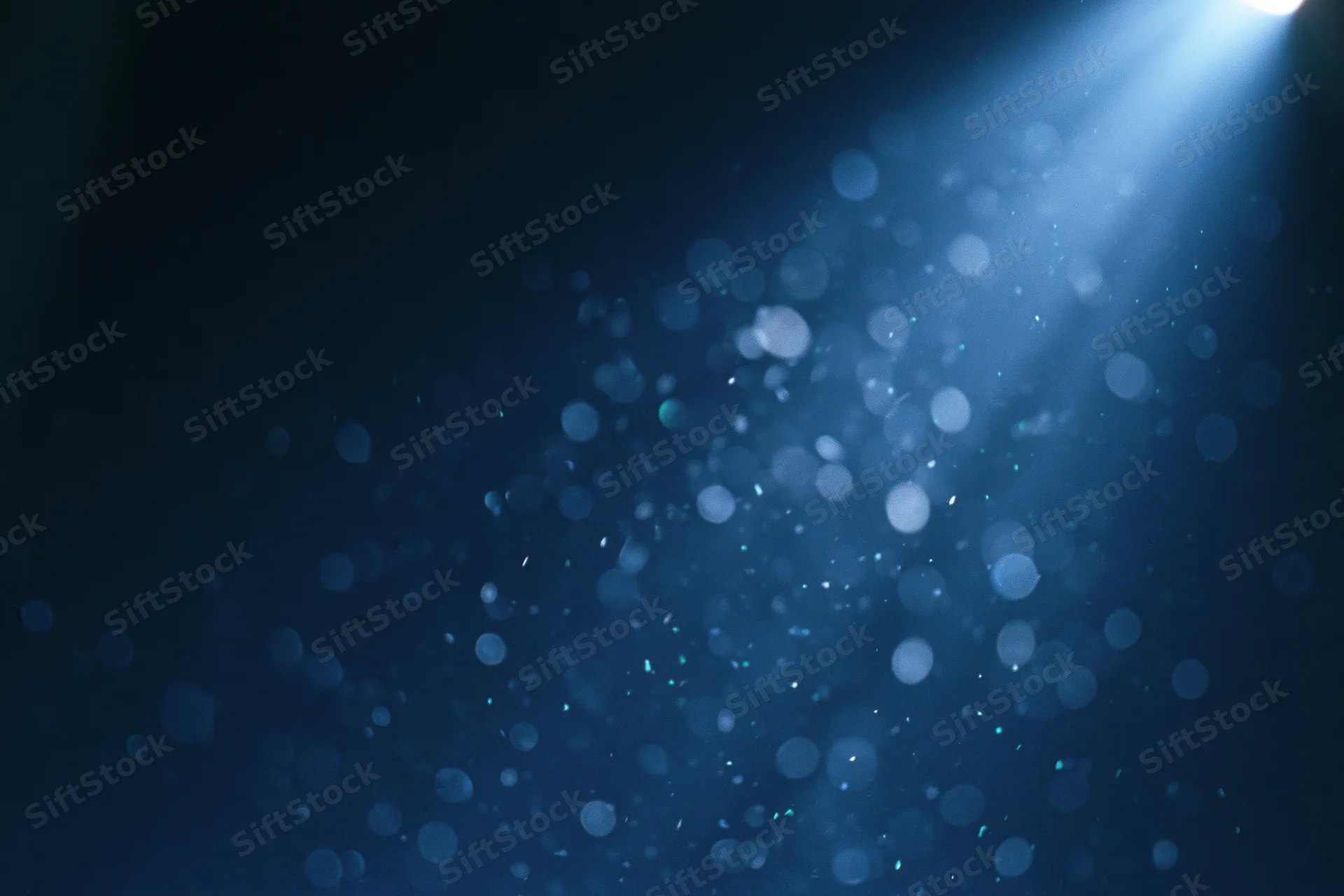 Floating out-of-focus light particles in dark blue abstract background with spotlight glow