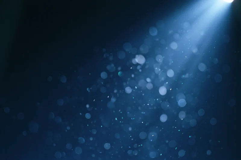 Floating out-of-focus light particles in dark blue abstract background with spotlight glow